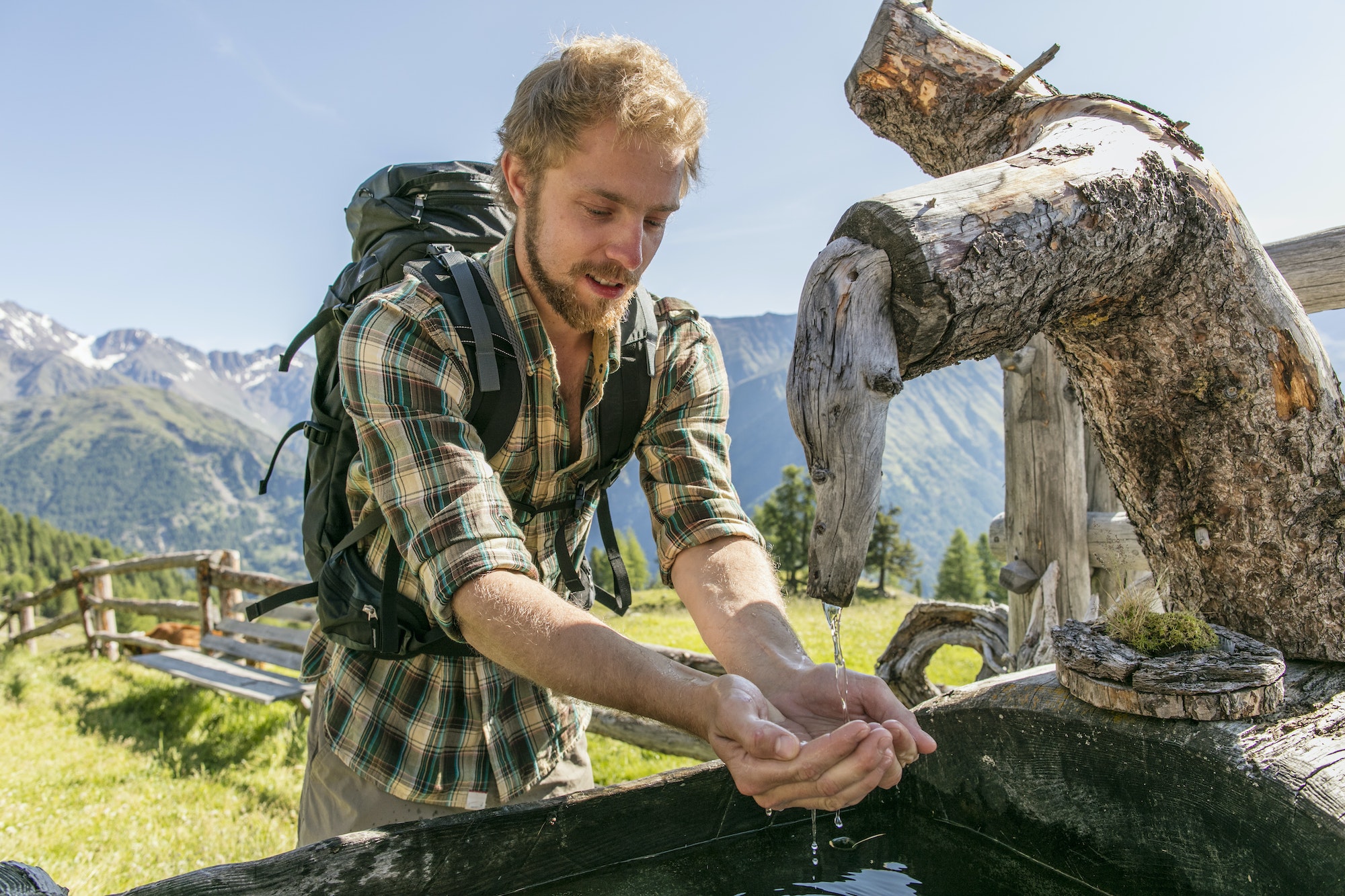 Young male hiker drinking water from rustic trough, Karthaus, Val Senales, South Tyrol, Italy